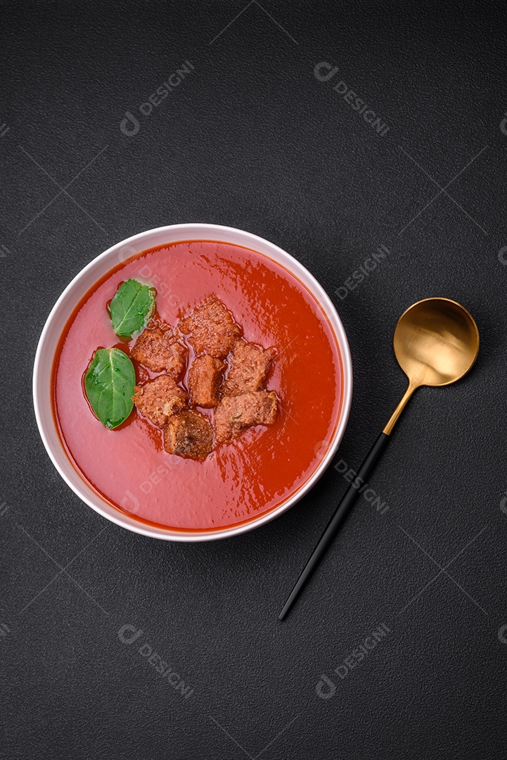 Delicioso gaspacho fresco com pão ralado, sal e especiarias numa placa cerâmica sobre um fundo escuro de concreto