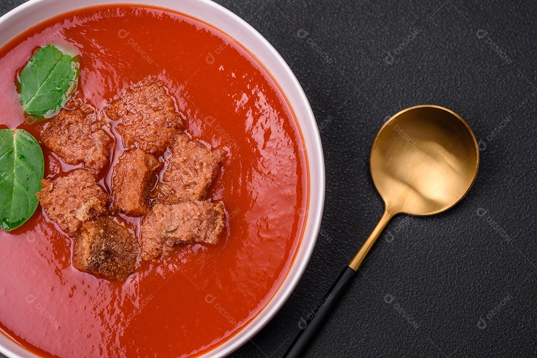 Delicioso gaspacho fresco com pão ralado, sal e especiarias numa placa cerâmica sobre um fundo escuro de concreto