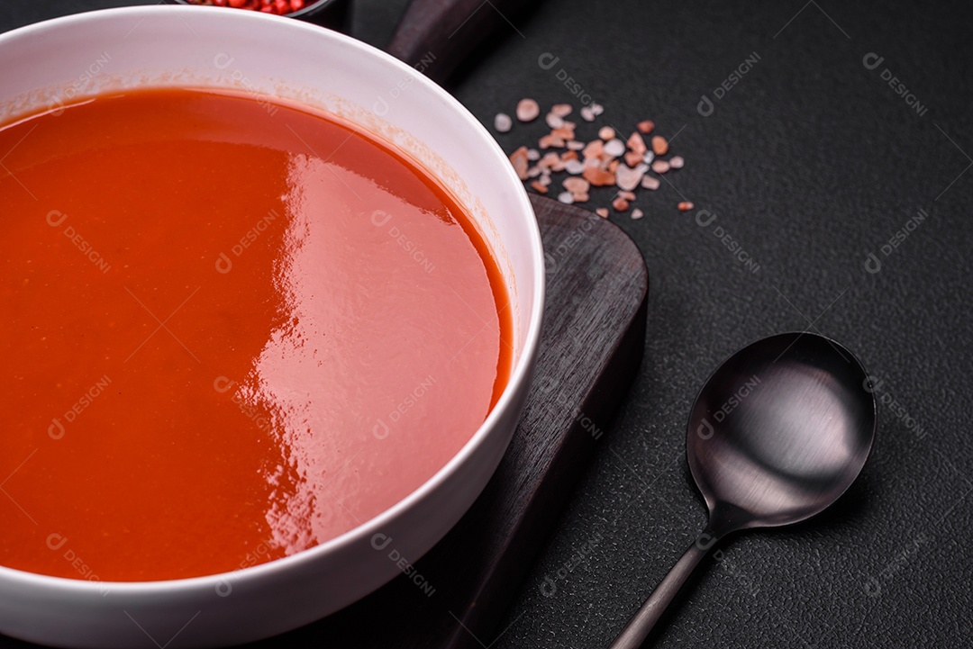 Delicioso gaspacho fresco com pão ralado, sal e especiarias numa placa cerâmica sobre um fundo escuro de concreto