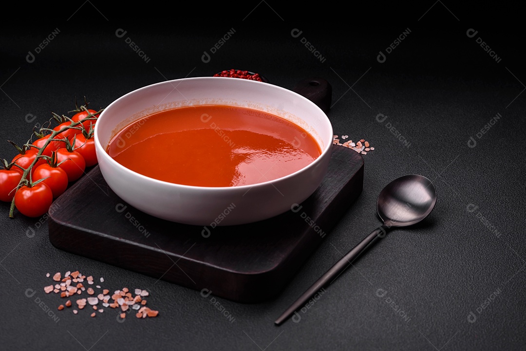 Delicioso gaspacho fresco com pão ralado, sal e especiarias numa placa cerâmica sobre um fundo escuro de concreto