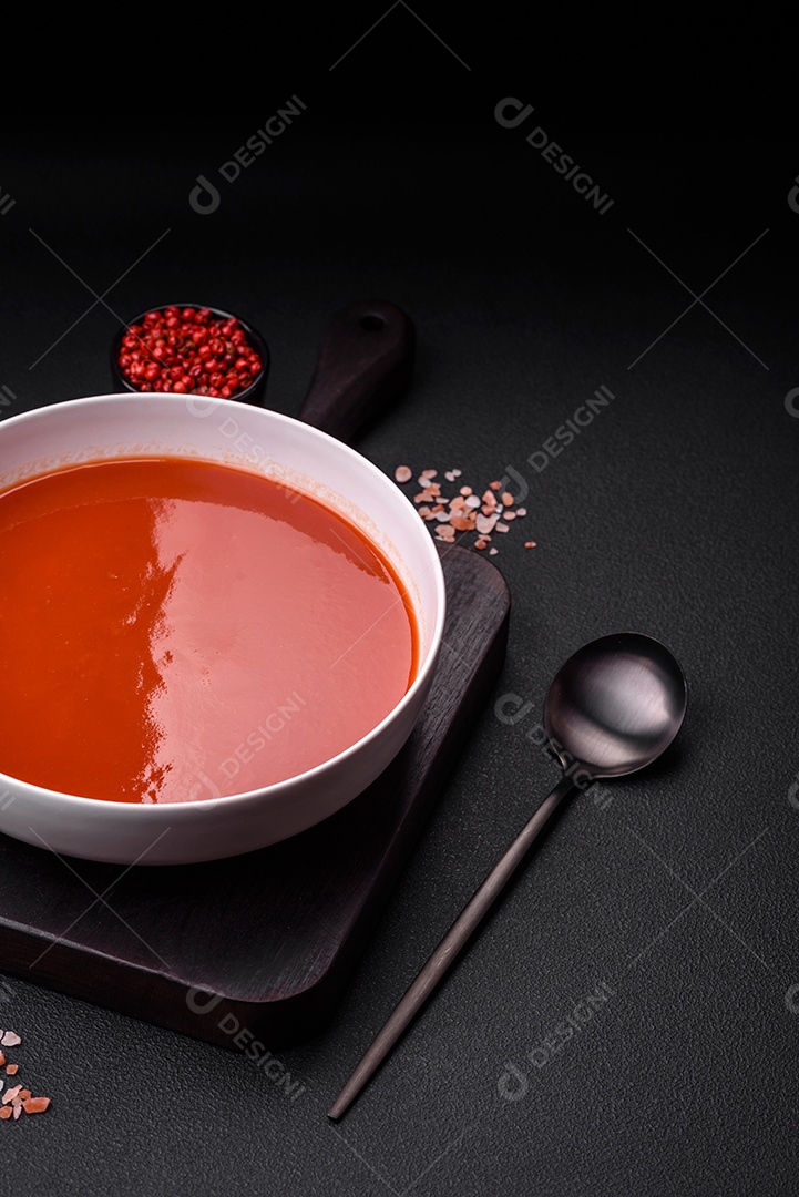 Delicioso gaspacho fresco com pão ralado, sal e especiarias numa placa cerâmica sobre um fundo escuro de concreto