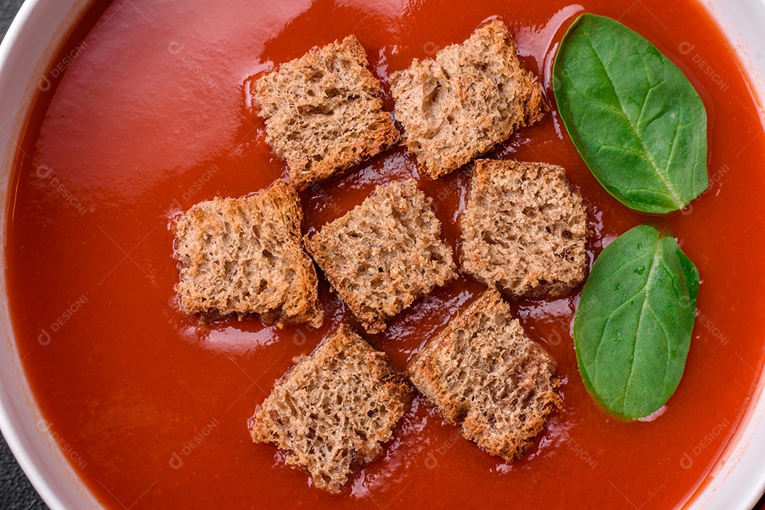 Delicioso gaspacho fresco com pão ralado, sal e especiarias numa placa cerâmica sobre um fundo escuro de concreto
