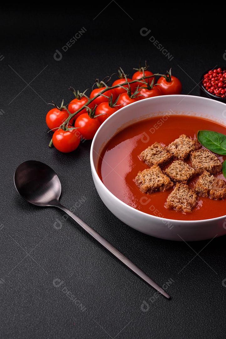 Delicioso gaspacho fresco com pão ralado, sal e especiarias numa placa cerâmica sobre um fundo escuro de concreto