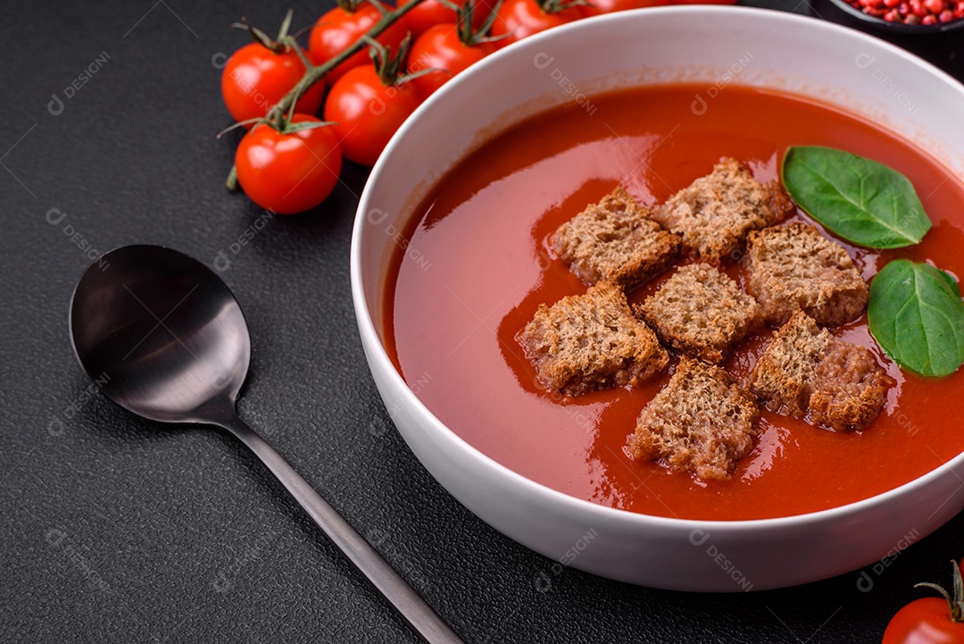 Delicioso gaspacho fresco com pão ralado, sal e especiarias numa placa cerâmica sobre um fundo escuro de concreto