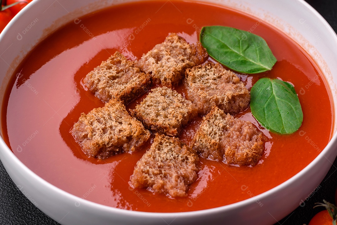 Delicioso gaspacho fresco com pão ralado, sal e especiarias numa placa cerâmica sobre um fundo escuro de concreto