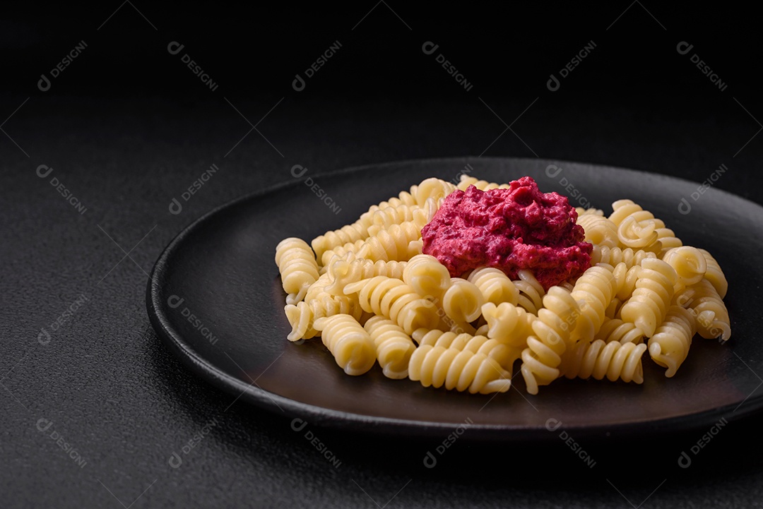 Deliciosa massa fusilli com pesto de beterraba, parmesão, sal e especiarias sobre um fundo escuro de concreto