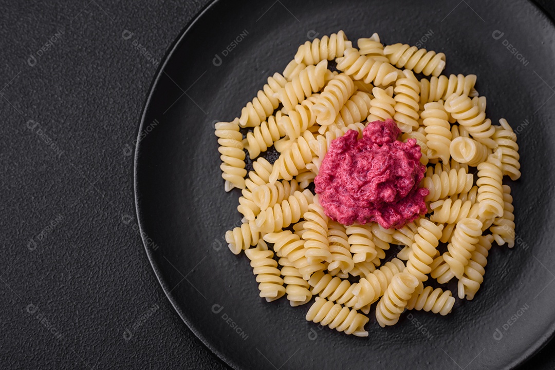 Deliciosa massa fusilli com pesto de beterraba, parmesão, sal e especiarias sobre um fundo escuro de concreto