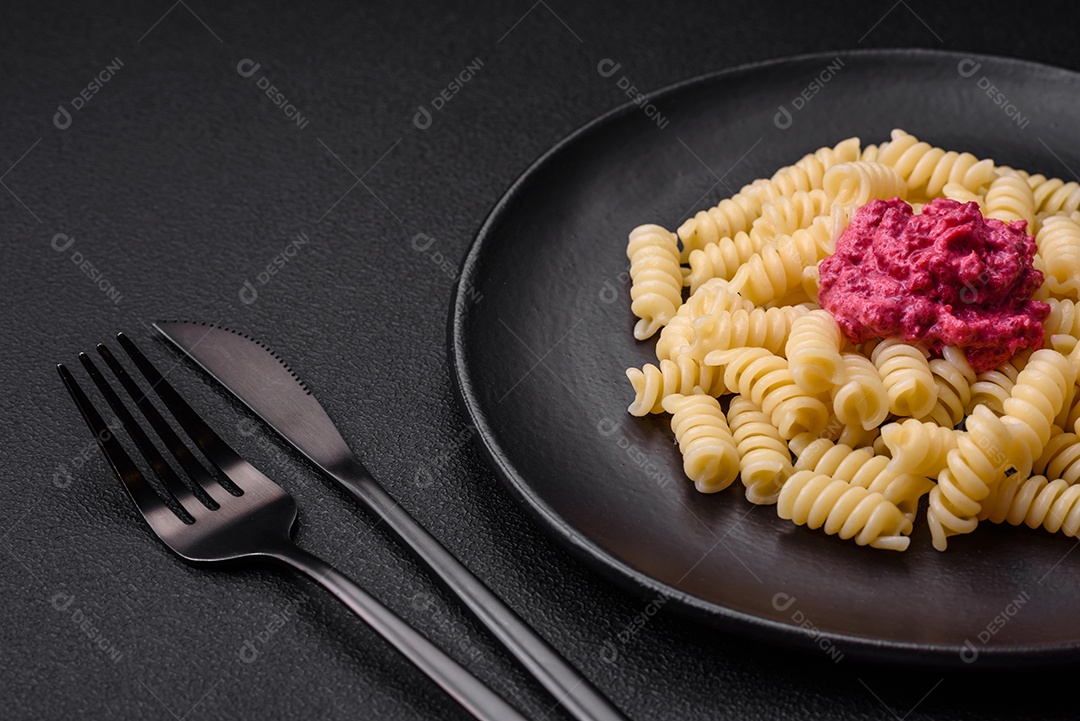 Deliciosa massa fusilli com pesto de beterraba, parmesão, sal e especiarias sobre um fundo escuro de concreto