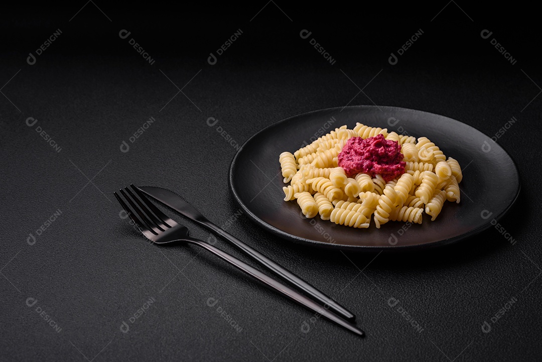 Deliciosa massa fusilli com pesto de beterraba, parmesão, sal e especiarias sobre um fundo escuro de concreto
