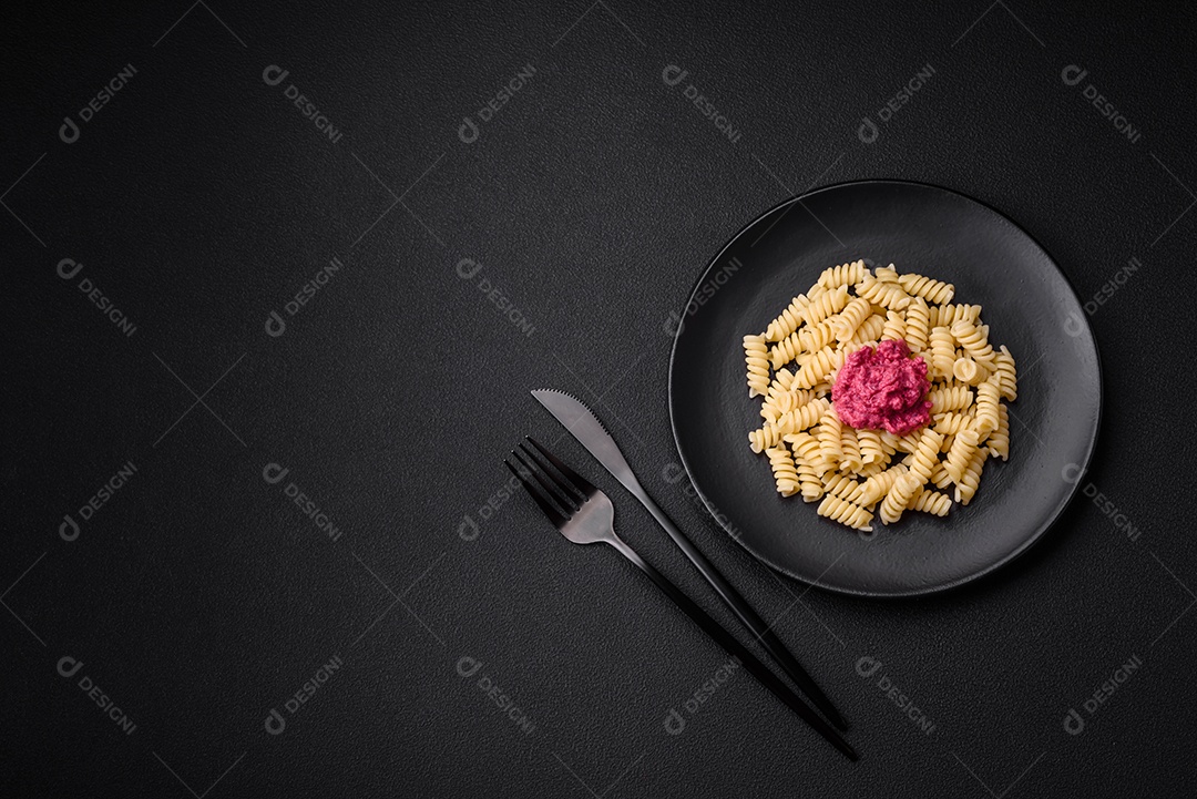 Deliciosa massa fusilli com pesto de beterraba, parmesão, sal e especiarias sobre um fundo escuro de concreto