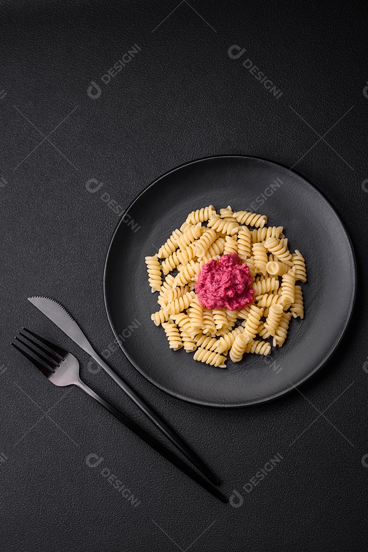 Deliciosa massa fusilli com pesto de beterraba, parmesão, sal e especiarias sobre um fundo escuro de concreto