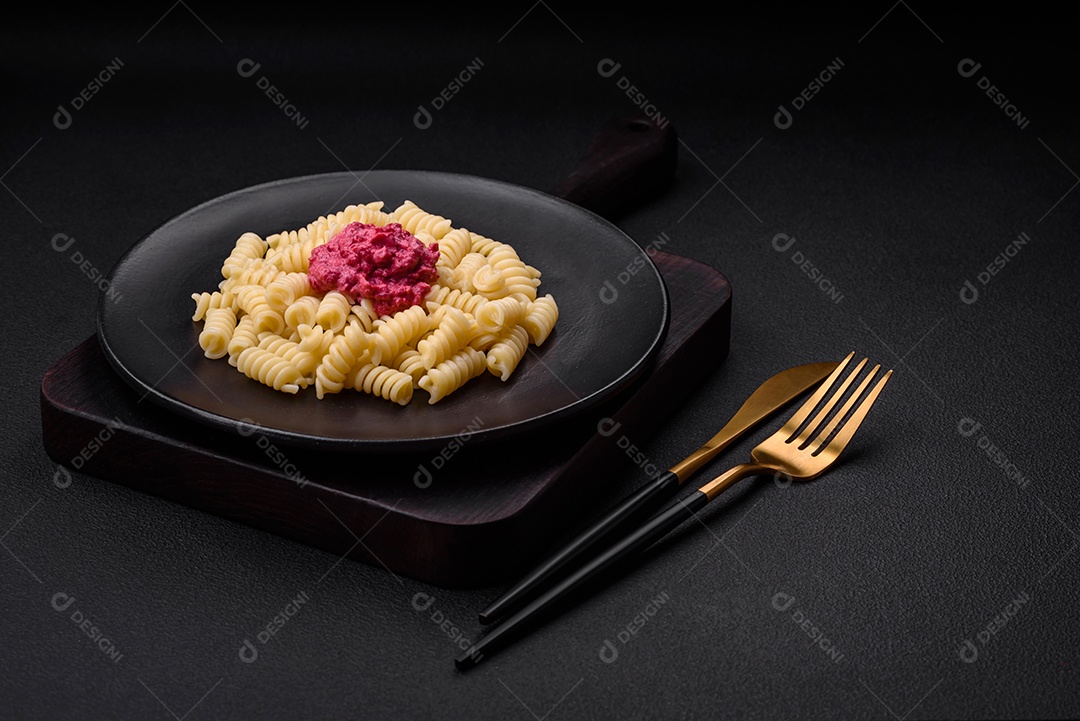 Deliciosa massa fusilli com pesto de beterraba, parmesão, sal e especiarias sobre um fundo escuro de concreto