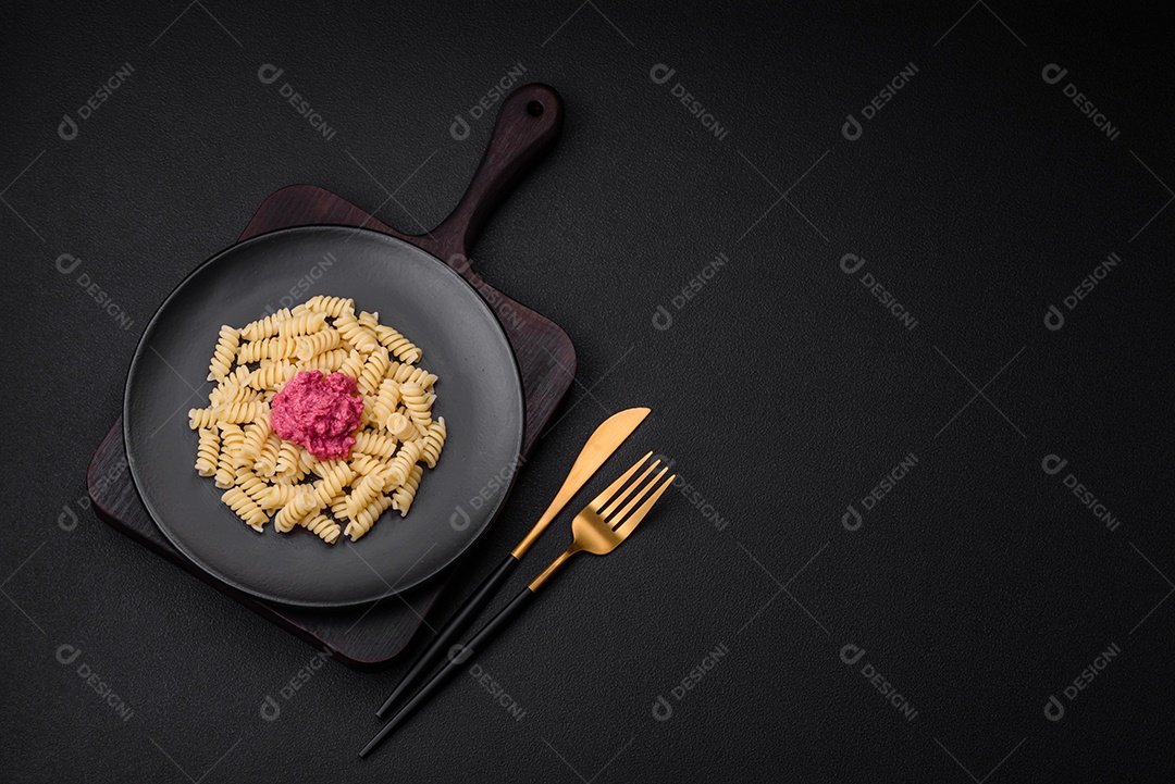 Deliciosa massa fusilli com pesto de beterraba, parmesão, sal e especiarias sobre um fundo escuro de concreto