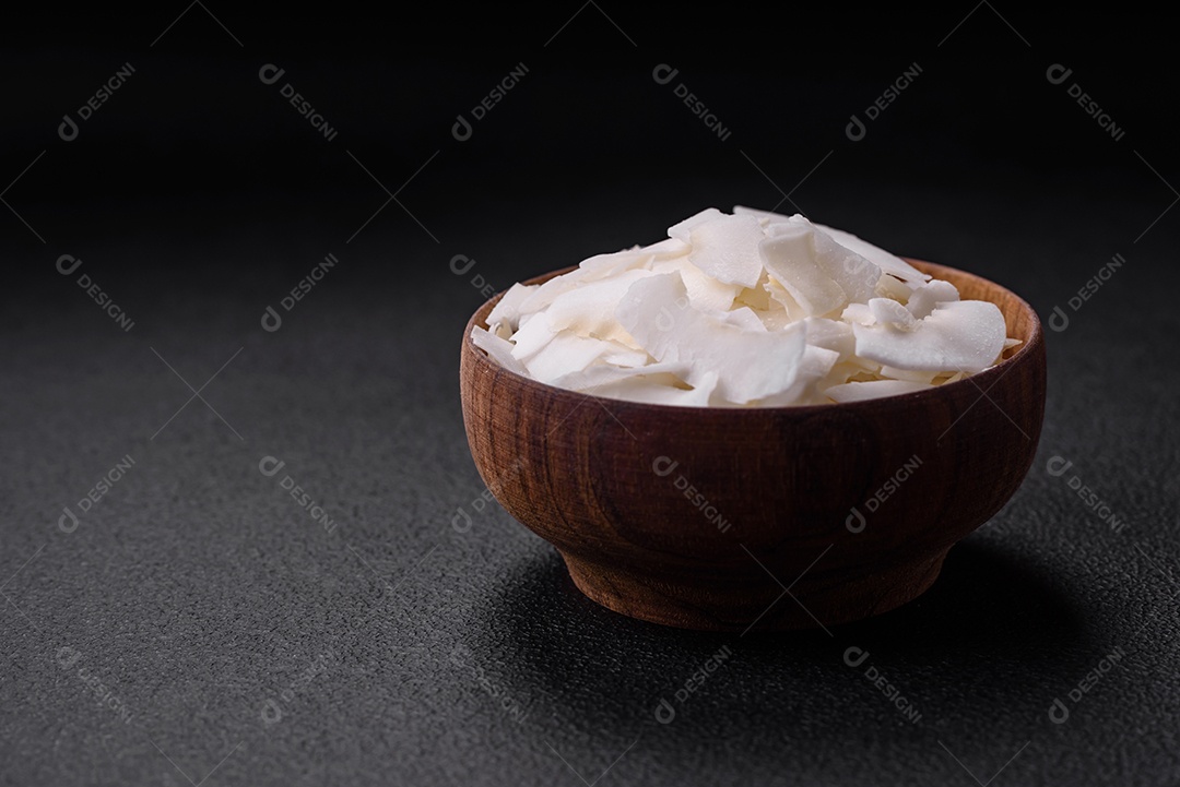 Flocos de coco branco seco em uma tigela de madeira preparada para fazer sobremesas sobre um fundo de concreto texturizado