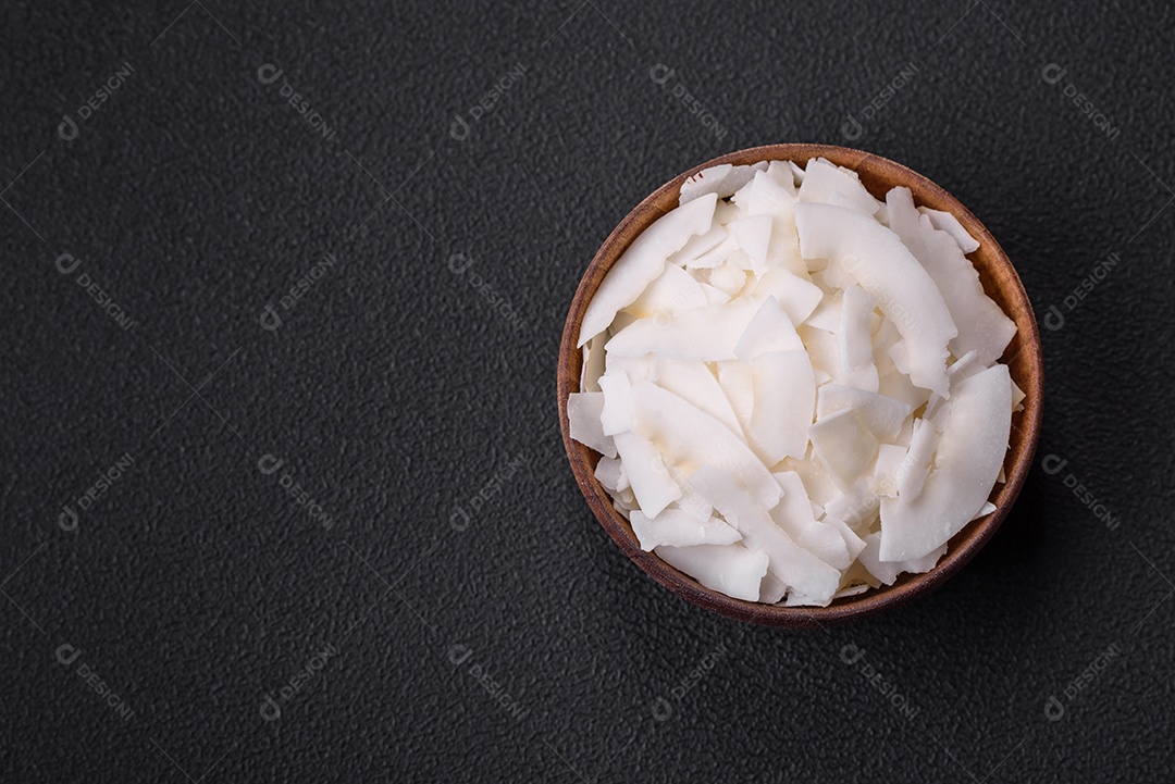Flocos de coco branco seco em uma tigela de madeira preparada para fazer sobremesas sobre um fundo de concreto texturizado