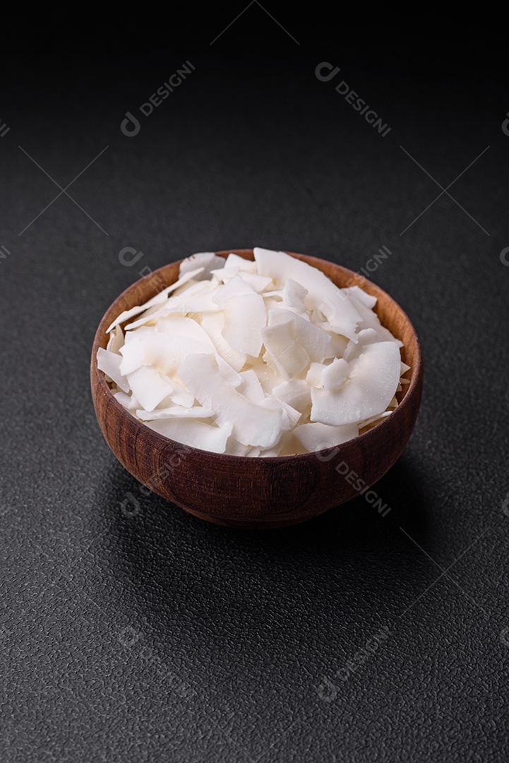 Flocos de coco branco seco em uma tigela de madeira preparada para fazer sobremesas sobre um fundo de concreto texturizado