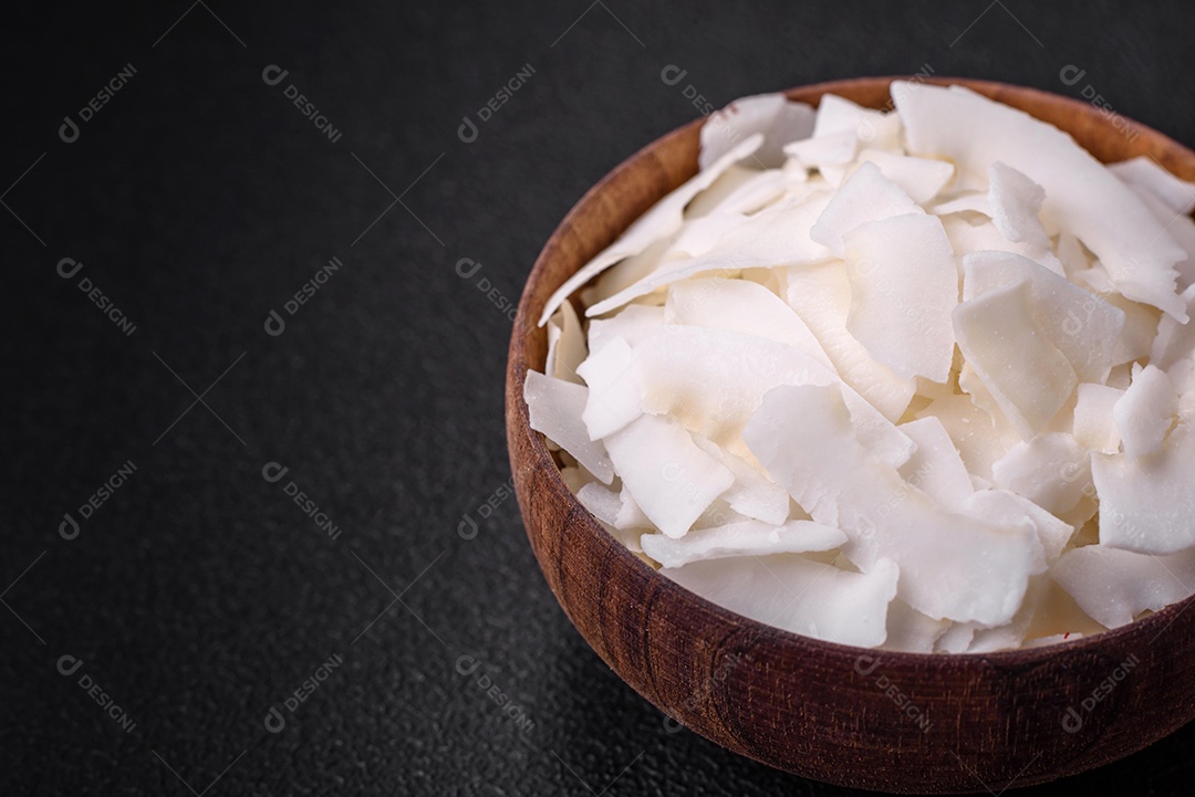 Flocos de coco branco seco em uma tigela de madeira preparada para fazer sobremesas sobre um fundo de concreto texturizado