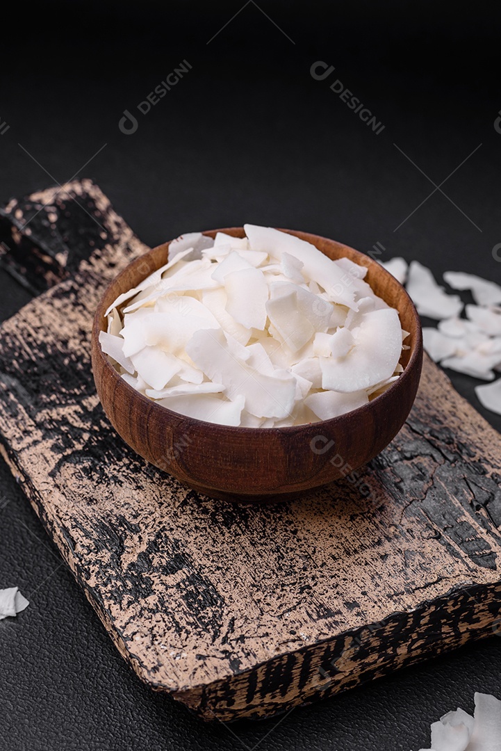Flocos de coco branco seco em uma tigela de madeira preparada para fazer sobremesas sobre um fundo de concreto texturizado
