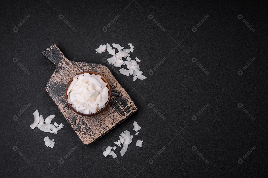 Flocos de coco branco seco em uma tigela de madeira preparada para fazer sobremesas sobre um fundo de concreto texturizado
