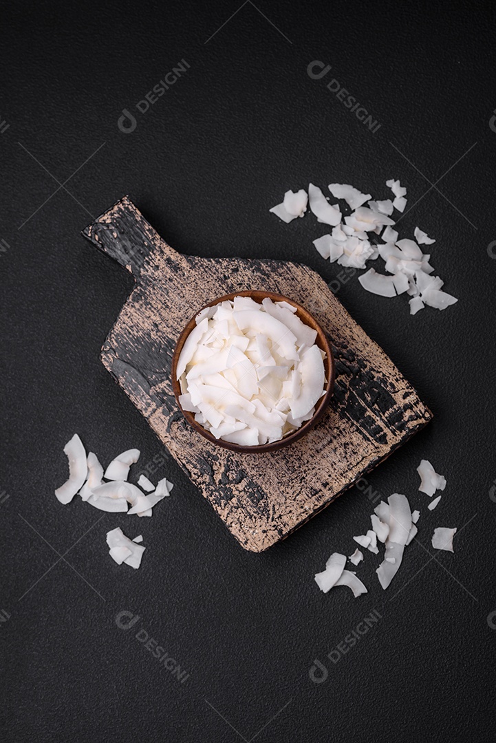 Flocos de coco branco seco em uma tigela de madeira preparada para fazer sobremesas sobre um fundo de concreto texturizado