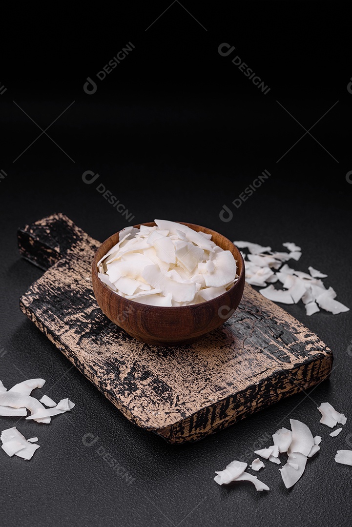 Flocos de coco branco seco em uma tigela de madeira preparada para fazer sobremesas sobre um fundo de concreto texturizado