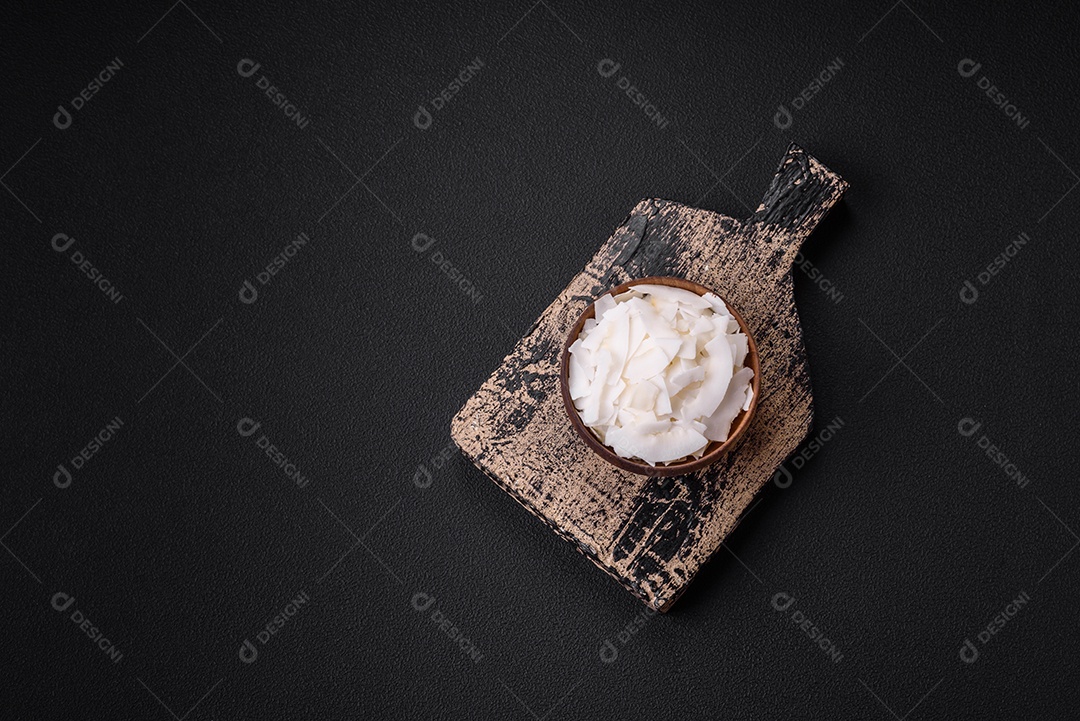 Flocos de coco branco seco em uma tigela de madeira preparada para fazer sobremesas sobre um fundo de concreto texturizado