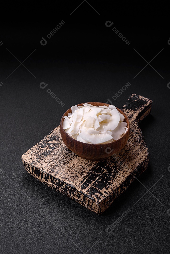 Flocos de coco branco seco em uma tigela de madeira preparada para fazer sobremesas sobre um fundo de concreto texturizado