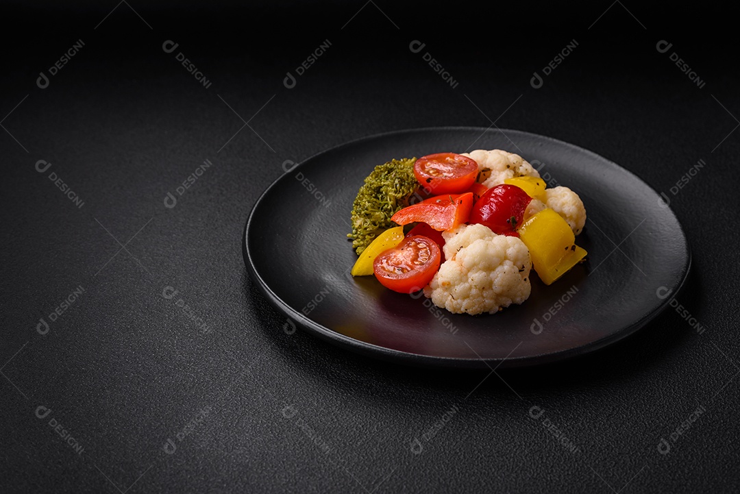 Deliciosa salada fresca de brócolis, couve-flor, pimentão e tomate cereja com especiarias e sal sobre um fundo escuro de concreto