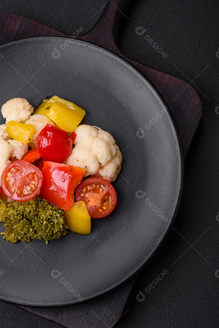 Deliciosa salada fresca de brócolis, couve-flor, pimentão e tomate cereja com especiarias e sal sobre um fundo escuro de concreto