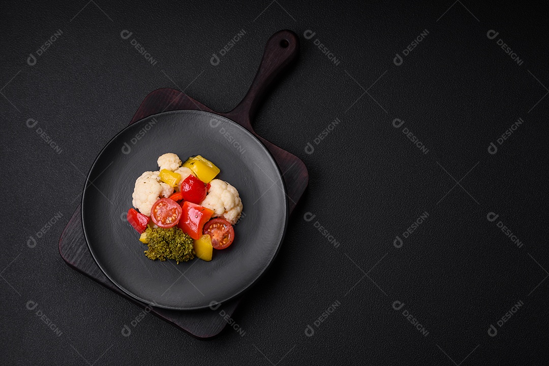 Deliciosa salada fresca de brócolis, couve-flor, pimentão e tomate cereja com especiarias e sal sobre um fundo escuro de concreto