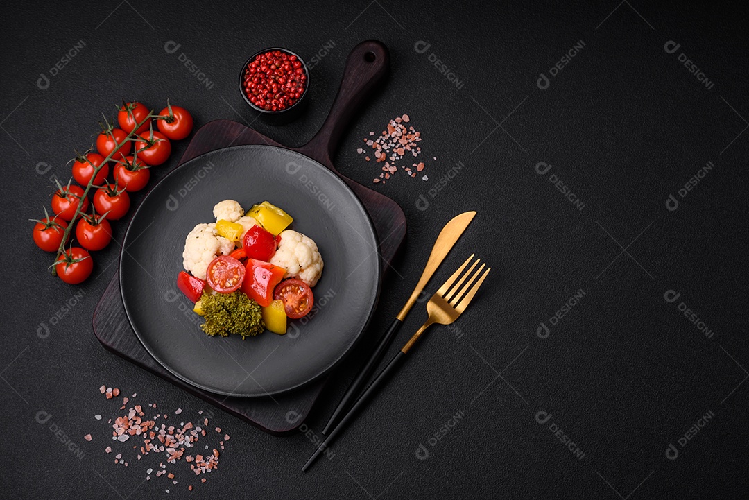 Deliciosa salada fresca de brócolis, couve-flor, pimentão e tomate cereja com especiarias e sal sobre um fundo escuro de concreto