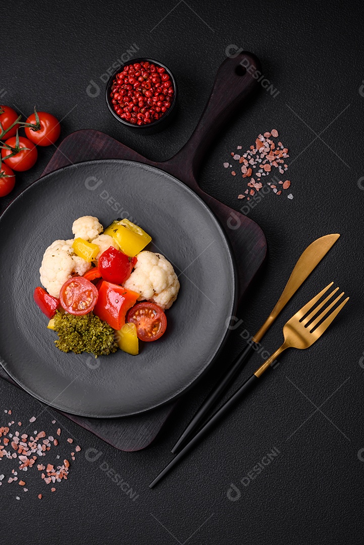 Deliciosa salada fresca de brócolis, couve-flor, pimentão e tomate cereja com especiarias e sal sobre um fundo escuro de concreto