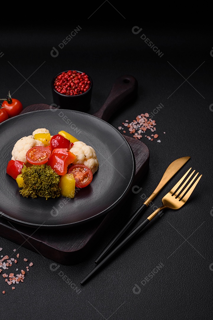 Deliciosa salada fresca de brócolis, couve-flor, pimentão e tomate cereja com especiarias e sal sobre um fundo escuro de concreto