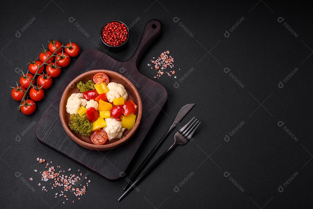 Deliciosa salada fresca de brócolis, couve-flor, pimentão e tomate cereja com especiarias e sal sobre um fundo escuro de concreto