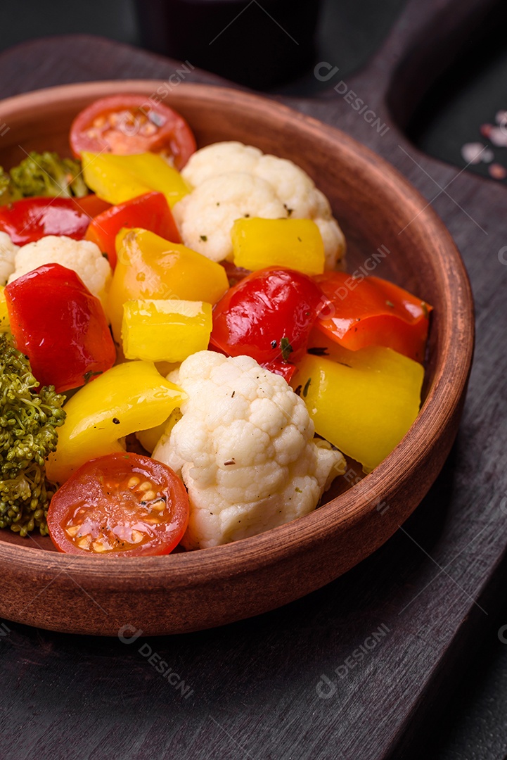 Deliciosa salada fresca de brócolis, couve-flor, pimentão e tomate cereja com especiarias e sal sobre um fundo escuro de concreto