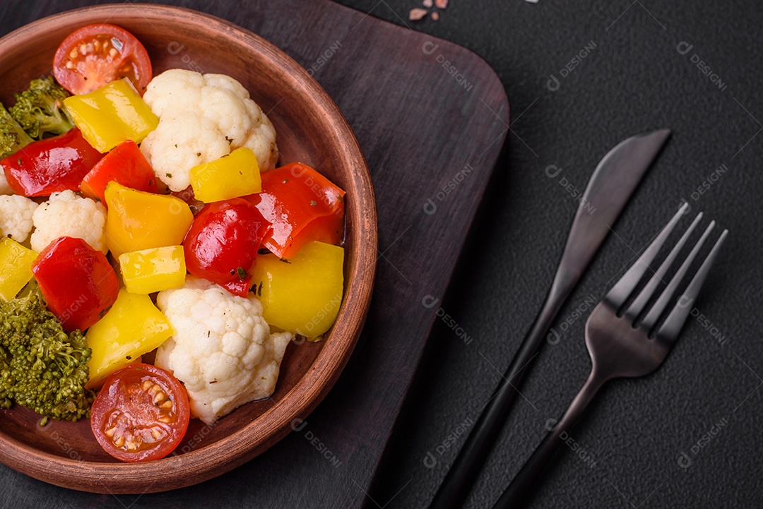 Deliciosa salada fresca de brócolis, couve-flor, pimentão e tomate cereja com especiarias e sal sobre um fundo escuro de concreto