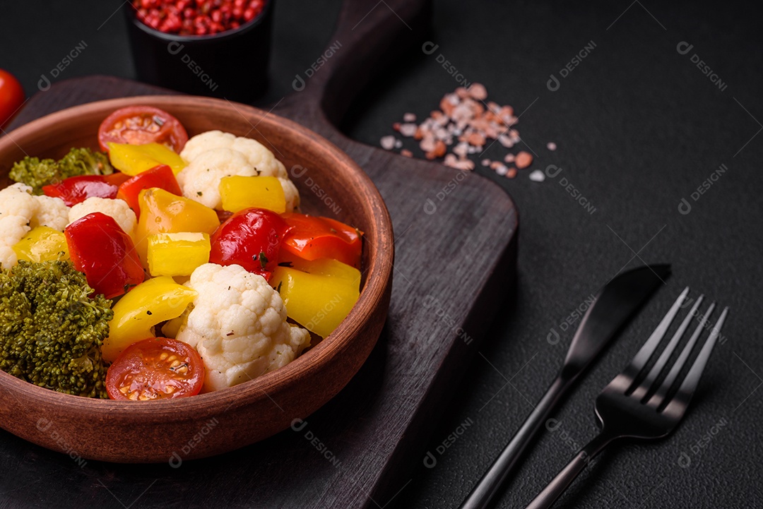 Deliciosa salada fresca de brócolis, couve-flor, pimentão e tomate cereja com especiarias e sal sobre um fundo escuro de concreto