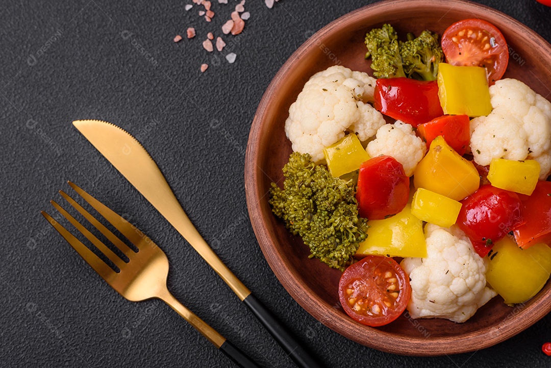 Deliciosa salada fresca de brócolis, couve-flor, pimentão e tomate cereja com especiarias e sal sobre um fundo escuro de concreto