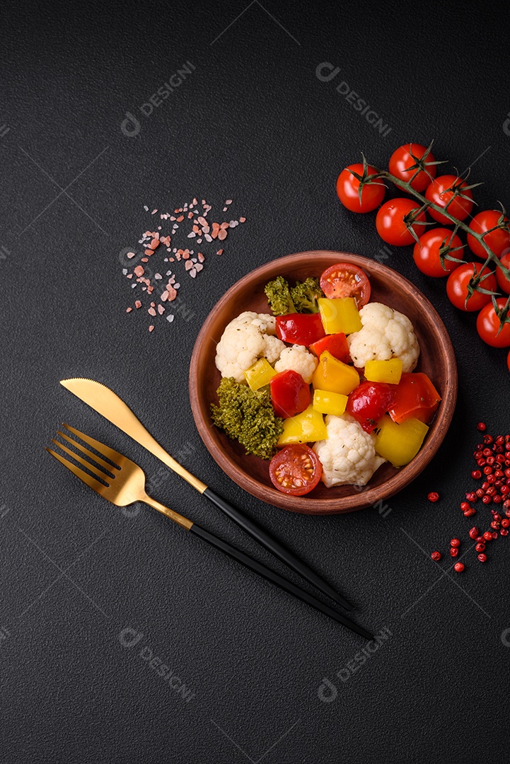 Deliciosa salada fresca de brócolis, couve-flor, pimentão e tomate cereja com especiarias e sal sobre um fundo escuro de concreto