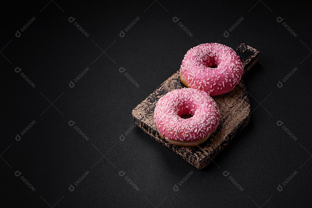 Deliciosos donuts doces frescos em esmalte rosa com recheio de morango sobre um fundo escuro de concreto