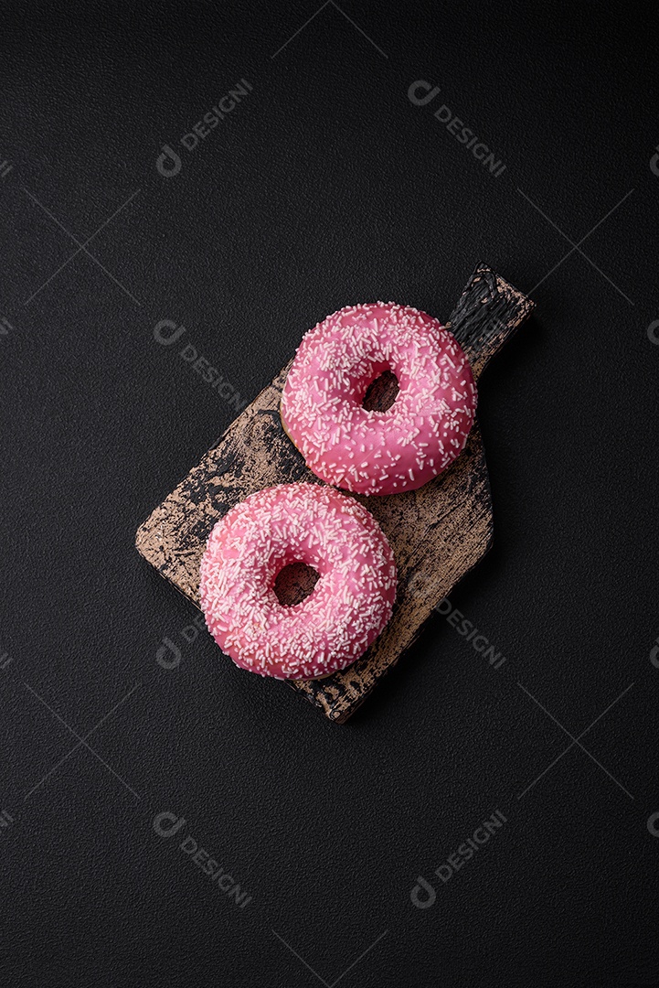 Deliciosos donuts doces frescos em esmalte rosa com recheio de morango sobre um fundo escuro de concreto