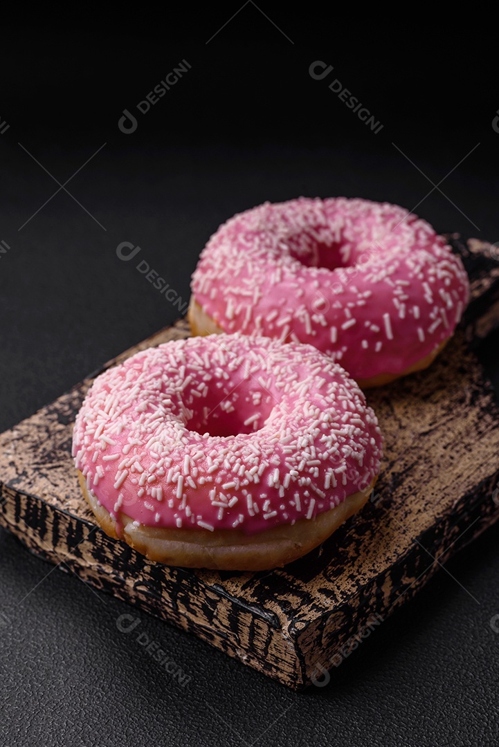 Deliciosos donuts doces frescos em esmalte rosa com recheio de morango sobre um fundo escuro de concreto