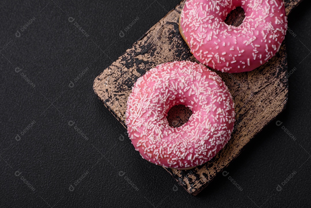 Deliciosos donuts doces frescos em esmalte rosa com recheio de morango sobre um fundo escuro de concreto