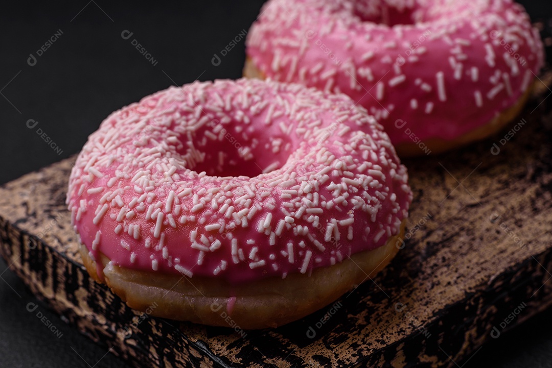 Deliciosos donuts doces frescos em esmalte rosa com recheio de morango sobre um fundo escuro de concreto