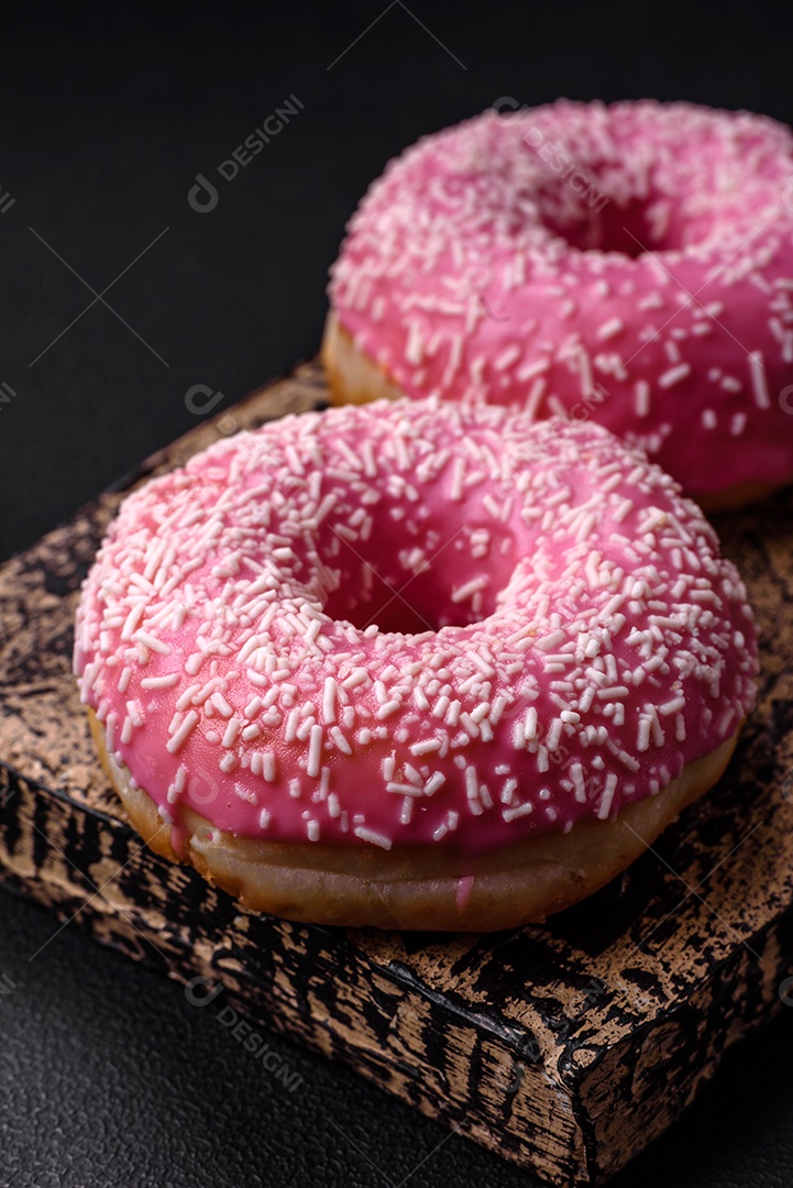 Deliciosos donuts doces frescos em esmalte rosa com recheio de morango sobre um fundo escuro de concreto
