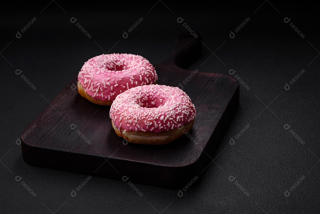 Deliciosos donuts doces frescos em esmalte rosa com recheio de morango sobre um fundo escuro de concreto