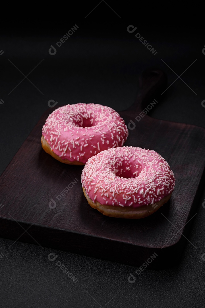 Deliciosos donuts doces frescos em esmalte rosa com recheio de morango sobre um fundo escuro de concreto