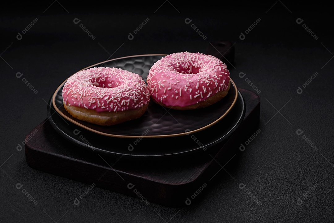 Deliciosos donuts doces frescos em esmalte rosa com recheio de morango sobre um fundo escuro de concreto