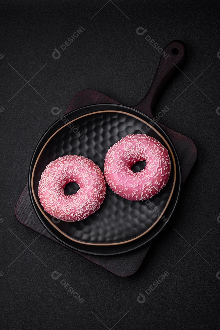 Deliciosos donuts doces frescos em esmalte rosa com recheio de morango sobre um fundo escuro de concreto
