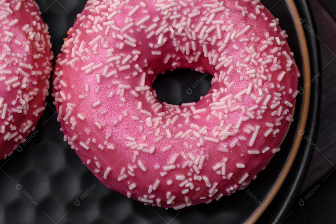 Deliciosos donuts doces frescos em esmalte rosa com recheio de morango sobre um fundo escuro de concreto